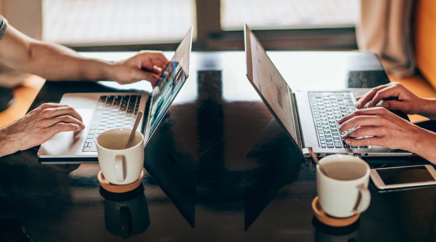 two people typing on laptops at black table